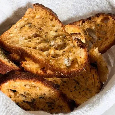 Crispy mini bruschetta with Sicilian oregano in a linen-lined bowl
